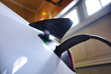 White EV electric car plugged and charging inside garage at home with green battery level indictor...