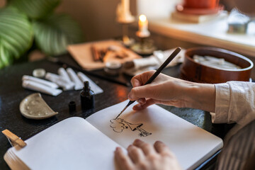 Close up of artist holding fountain pen drawing with ink while sitting at table with sketchbook and painting tools, drawing at home, creating artwork. Creative people and inspiration concept