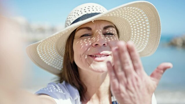 Middle age hispanic woman tourist smiling wearing summer hat taking selfie picture at the beach