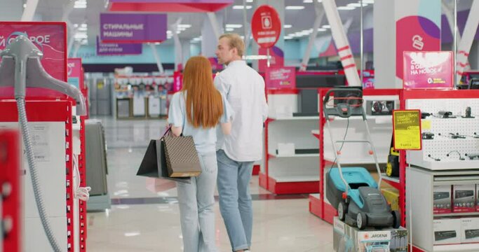 Young married couple man and woman walking in appliances store choosing a washing machine for the house. back rare view Slow motion, family walking through an electronics store