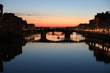 Naklejka premium Sunset over the River Arno in the summer. Beautiful Ponte Vecchio city. Night view of the old town country. Dusk over the medieval city. Natural beauty in the evening.