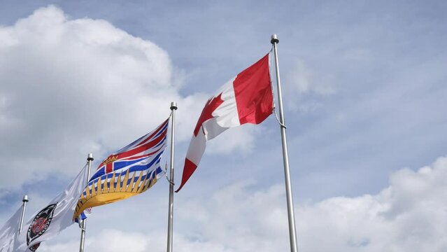 The flags of Canada and British Columbia waving in the wind against a blue cloudy sky at Whistler Village in Whistler, British Columbia, Canada.