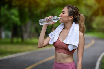 Young woman exercising, young woman drinking water and relaxing after morning workout with soft sunlight in public park