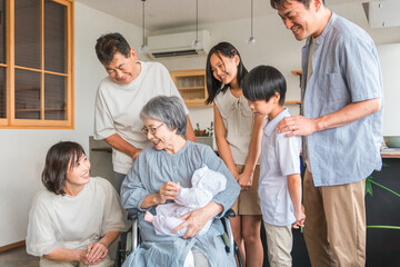 赤ちゃんと対面する車椅子に乗った高齢者女性と子供達・家族

