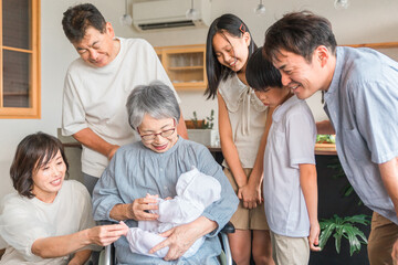 赤ちゃんと対面する車椅子に乗った高齢者女性と子供達・家族
