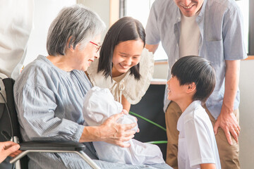 赤ちゃんと対面する車椅子に乗った高齢者女性と子供達・家族
