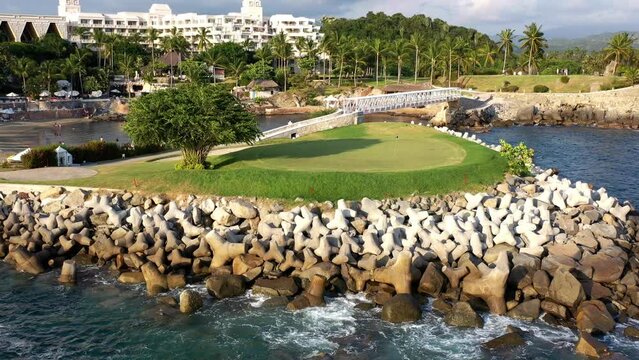 Toma de drone sobre campo de golf a la orilla del mar con un gran &aacute;rbol a la vista.