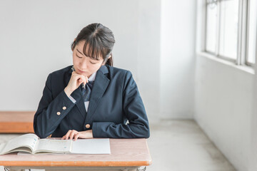 学校の教室で数学の教科書・参考書を見て悩みながら勉強する女子高校生・中学生の生徒（困る・難しい）
