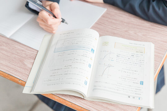 学校の教室で数学の教科書・参考書を見ながら勉強する女子高校生・中学生の生徒
