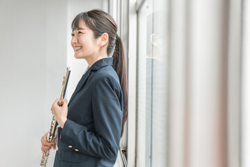 学校の教室でフルートを吹く吹奏楽部のアジア人女子高生

