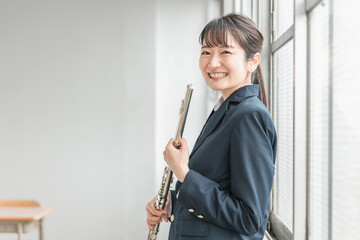 学校の教室でフルートを吹く吹奏楽部のアジア人女子高生
