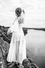 Fototapeta na wymiar A girl in a wedding dress stands on the edge of a cliff and stretches her hand towards her future happiness.