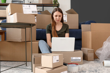 Young woman with parcels using laptop at home