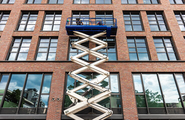 maintenance workers are repairing a modern building facade from an elevating scissor lift aerial...