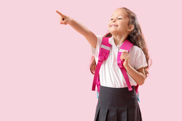 Little schoolgirl with backpack pointing at something on pink background - obrazy, fototapety, plakaty