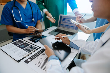 Medical team having a meeting with doctors in white lab coats and surgical scrubs seated at a table...