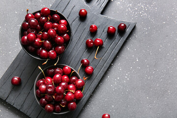 Board with bowls of sweet cherries on black table