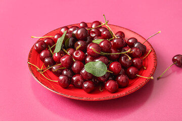 Plate of sweet cherries and leaves on pink background