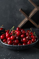 Bowl with sweet cherries on black background