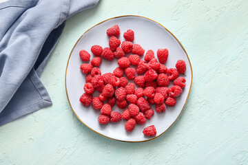 Plate with fresh raspberries on light blue background