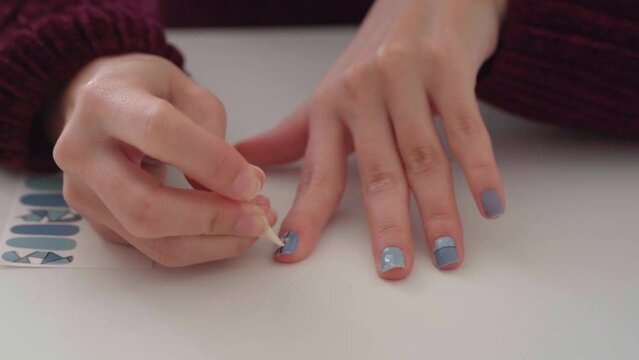 Woman applying nail decal sticker on her hands while doing her nails. Manicure and beauty concept.