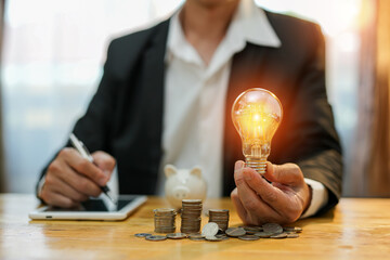 Business man holding light bulb on the Green background nature and writing on note book it for...