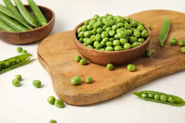 Bowls and wooden board with fresh green peas on white background