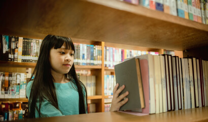 Little girl choosing book in public library room selecting literature for reading. girl chooses books on shelves learning from books is school education benefits of everyday reading concept.