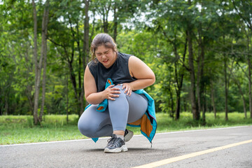 Overweight young woman with knee pain grabs her knee with both hands while sitting down at a running track of a local park