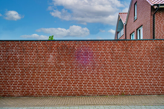 A tall red brick fence near a residential building in Germany