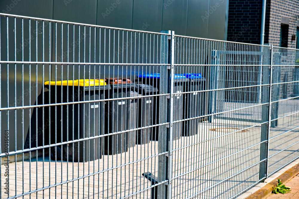 Poster fence with bunch of trash cans behind it and building in the background in germany.