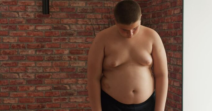 Upset plump shirtless boy after weighing. Teenage kid need to lose some excess weight. teen has problems with weight Slow motion depression kid cannot stop eating fast food and go in for sport illness