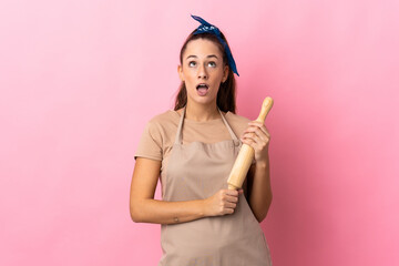Young woman holding a rolling pin looking up and with surprised expression