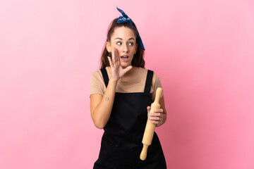 Young woman holding a rolling pin whispering something with surprise gesture while looking to the...