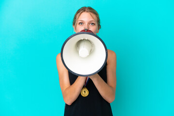 Young caucasian woman with medals isolated on blue background shouting through a megaphone