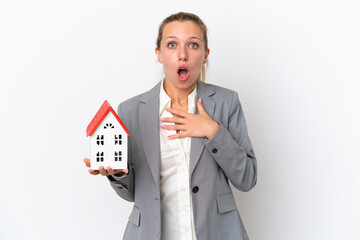 Real estate agent woman holding a toy house isolated on white background surprised and shocked...