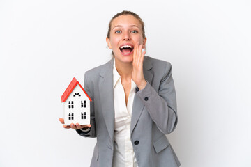 Real estate agent woman holding a toy house isolated on white background shouting with mouth wide...