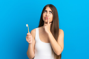 Young caucasian woman brushing teeth isolated on blue background having doubts while looking up