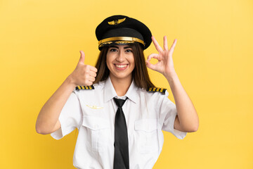 Airplane pilot isolated on yellow background showing ok sign and thumb up gesture
