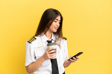 Airplane pilot isolated on yellow background holding coffee to take away and a mobile