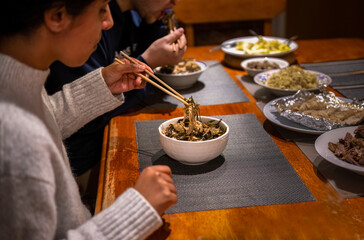 Fototapeta na wymiar Couple holding chopsticks and eating dinner. Vegetable and beef dishes on the dinner table. Home cooking and eating concept.