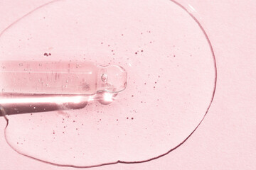 Glass dropper with liquid transparent serum on a pink background. Body care concept. Hyaluronic gel for skin.