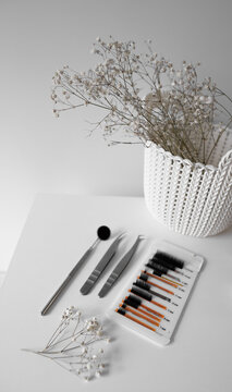 Tools of a professional lashmaker for eyelash extensions in a beauty salon. Artificial eyelashes next to tweezers and a mirror for eyelash extension procedure.