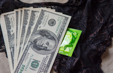 100 dollar bills and condoms in a package lie on black lace women's panties
