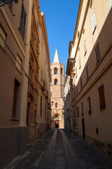 Fototapeta na wymiar Old street with church tower and stone houses in Alghero city on Sardinia island, Italy.