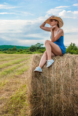 A girl sits on a haystack. Rest in the village. Farming.