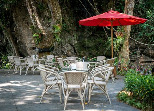the tables and chairs outside under a red umbrella are in front of trees