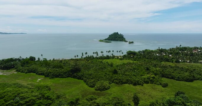 Aerial view of tropical island with green trees under clear sky and clouds. Davao Oriental, Philippines.