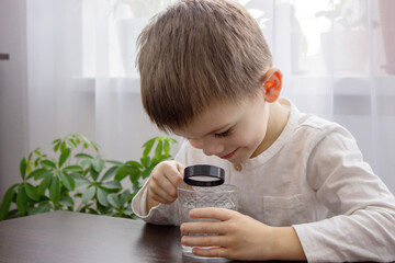 the child looks at the water through a magnifying glass. Selective focus.