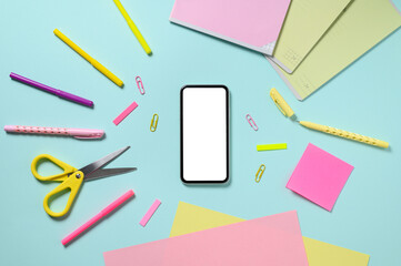 Smartphone with a blank white display and a lot of stationery items on a blue background. The concept of an online store for preparing for school. View from above
